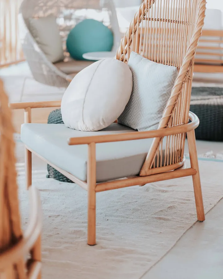 Un fauteuil en rotin garni de coussins, dans une pièce lumineuse